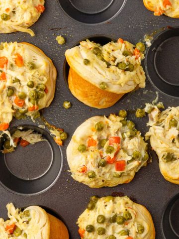 Baked mini chicken pot pies in biscuit cups resting in a muffin pan with golden edges and visible peas and carrots.
