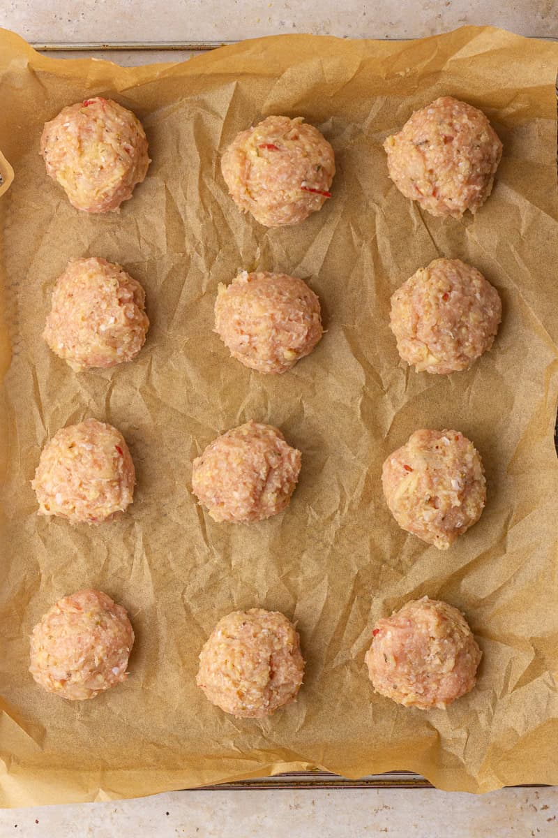 Evenly portioned meatball scoops lined up on a parchment-lined sheet pan.