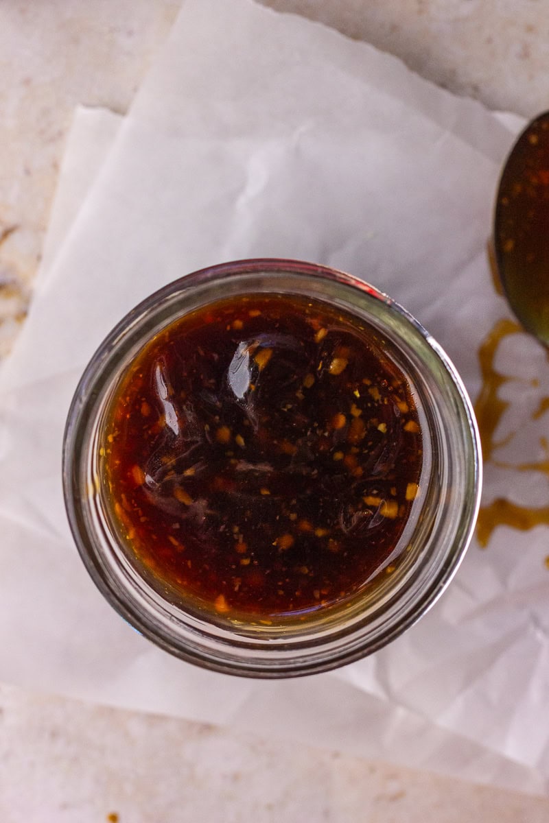 Overhead view of a mason jar filled with thick bourbon teriyaki sauce sitting on parchment paper.