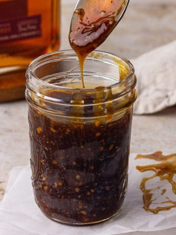A close up shows a mason jar filled with bourbon teriyaki sauce as a spoon lifts a silky drizzle.