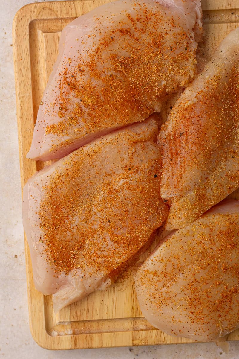 Raw chicken breasts on a cutting board sprinkled with paprika, salt, and pepper.
