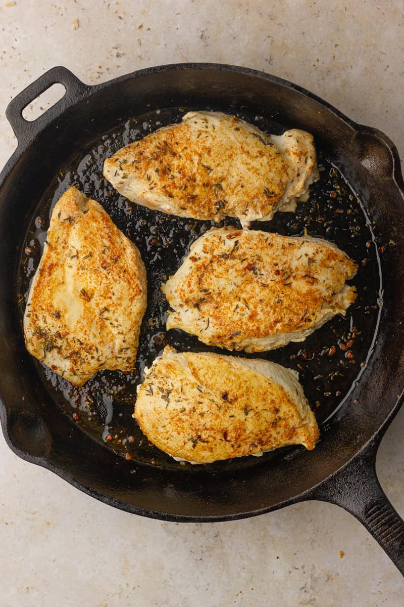 Golden-seared chicken breasts in a hot cast-iron skillet after the first sauté.
