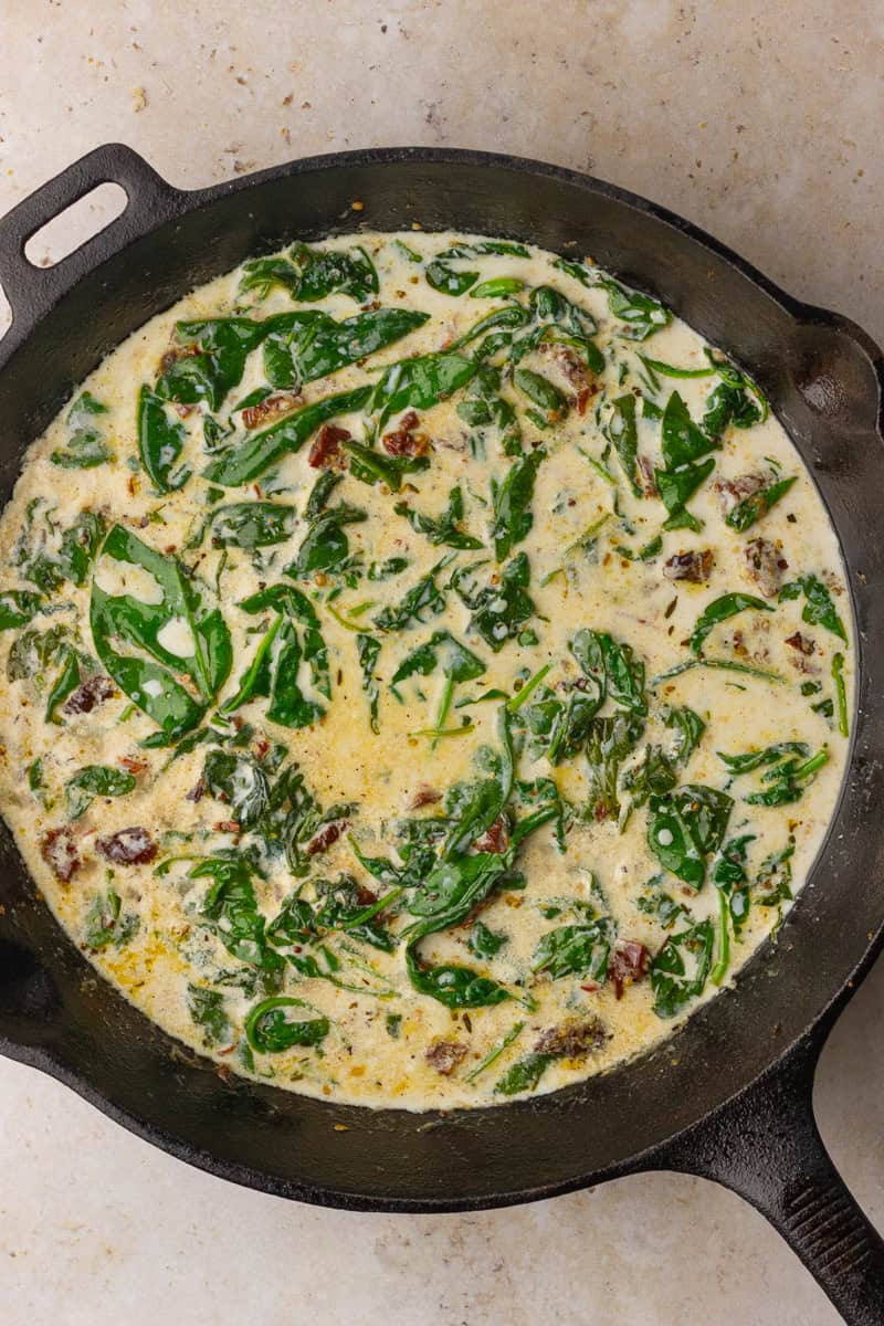 Creamy spinach and sun-dried tomato sauce gently bubbling in a cast-iron skillet.