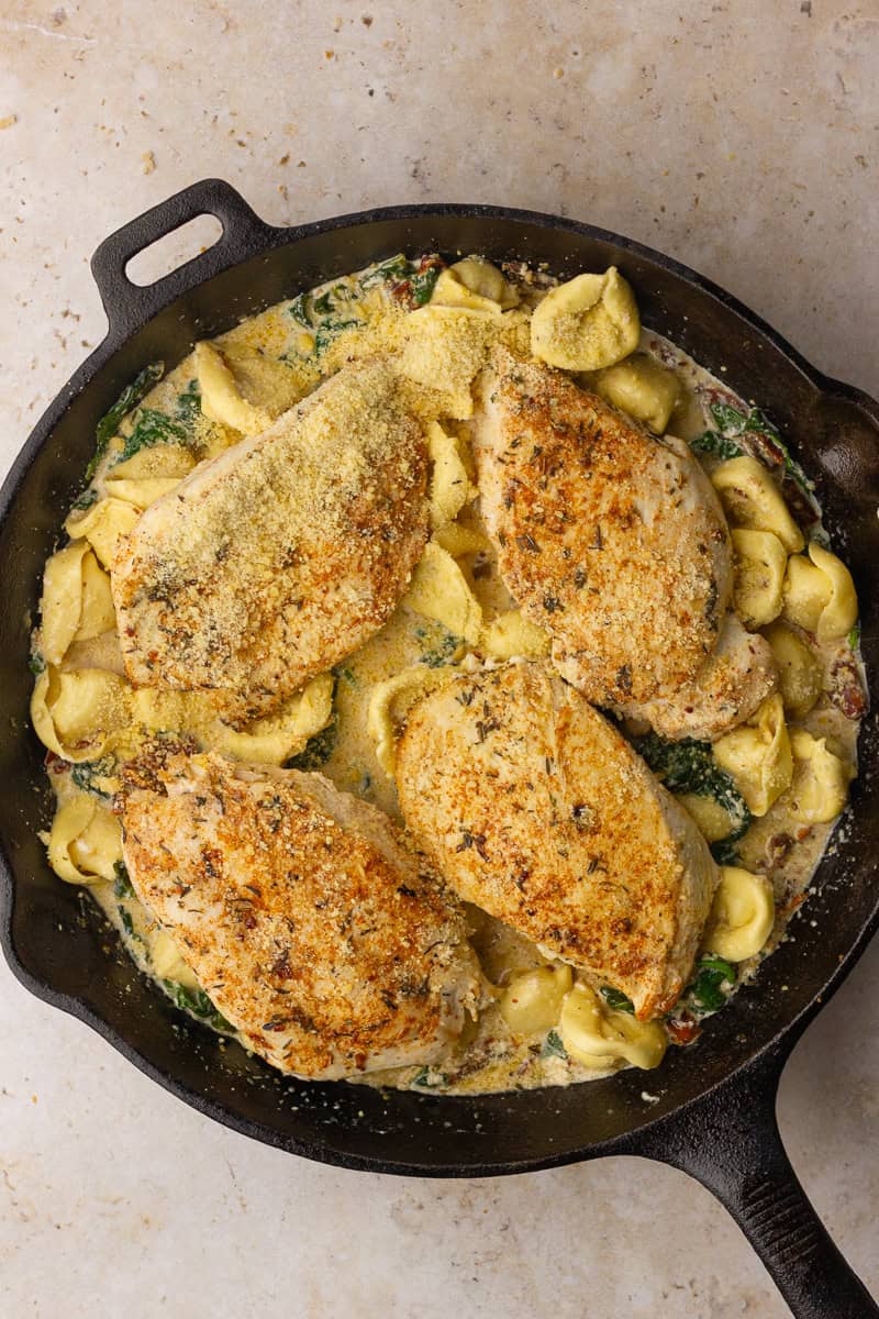 Assembled one-skillet bake ready to be baked with tortellini and seared chicken breasts topped with parmesan.