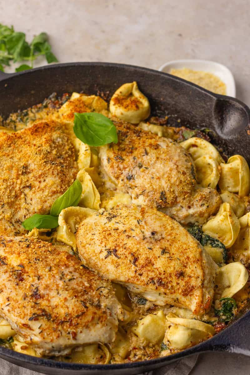Finished chicken tortellini bake, golden and bubbly in cast iron with fresh basil.