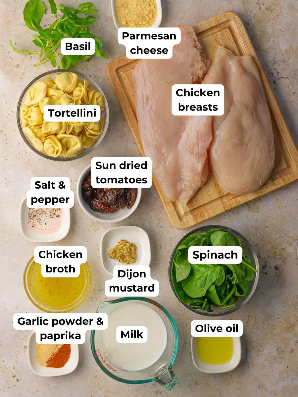 Overhead layout of labeled ingredients for chicken tortellini bake, including chicken, tortellini, spinach, milk, broth, and seasonings.