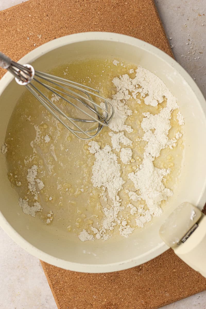 Melted butter and flour are being whisked together in a saucepan to form a roux.