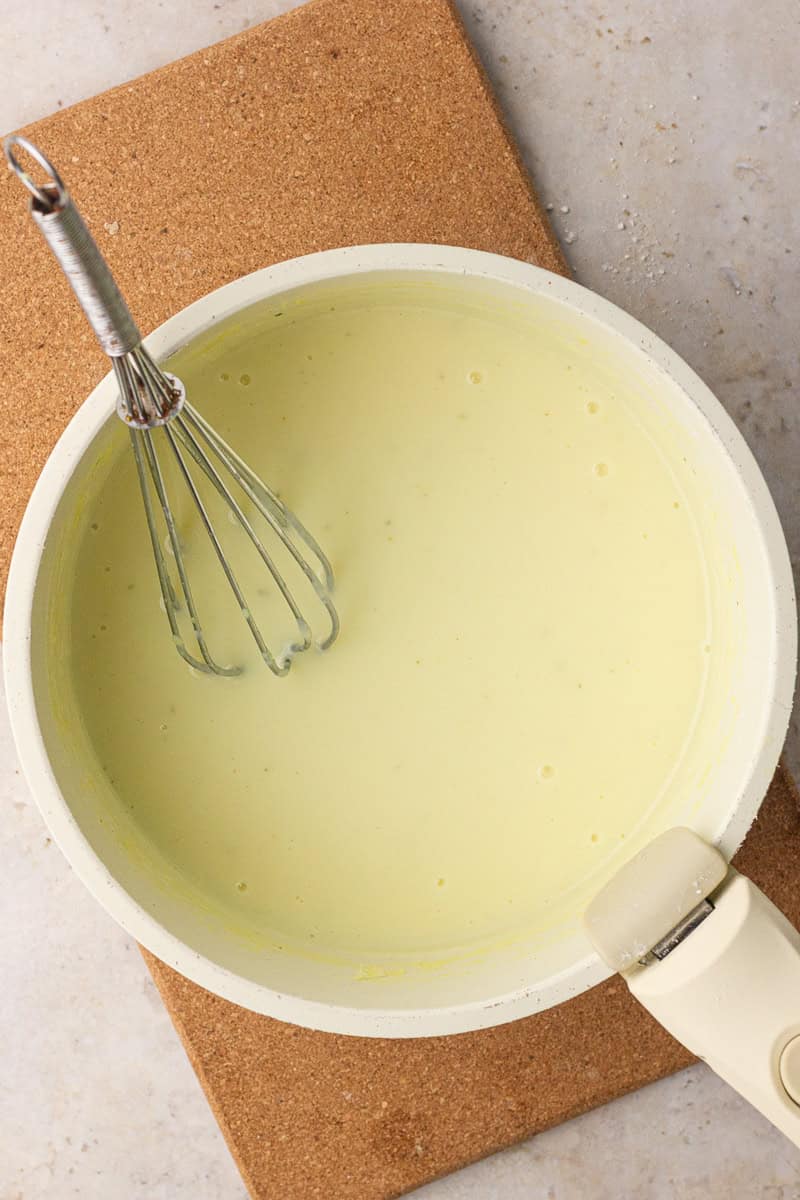 A pale yellow broth-and-milk mixture is whisked smooth in a saucepan before thickening.