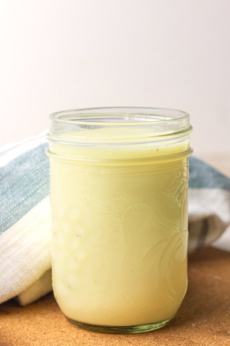 A glass mason jar filled with creamy homemade cream of chicken substitute sits on a cork trivet beside a striped towel.
