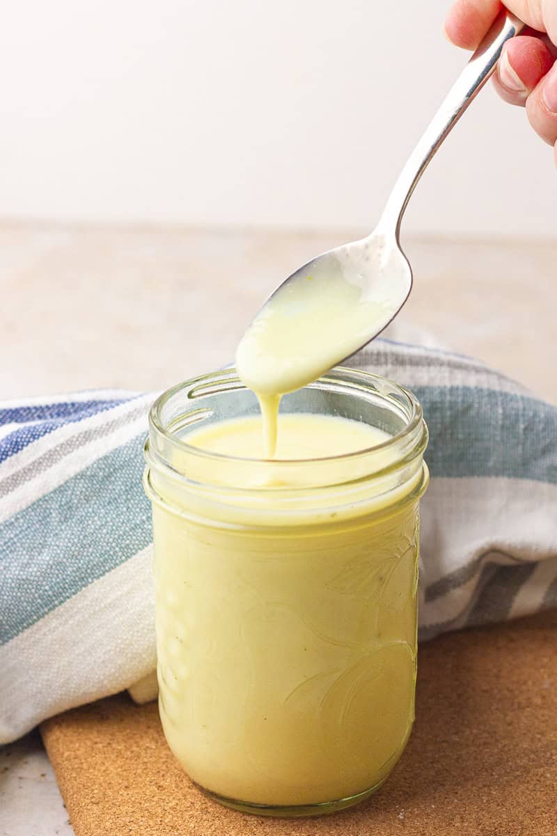 A spoon drizzles the thick, creamy substitute back into a mason jar.