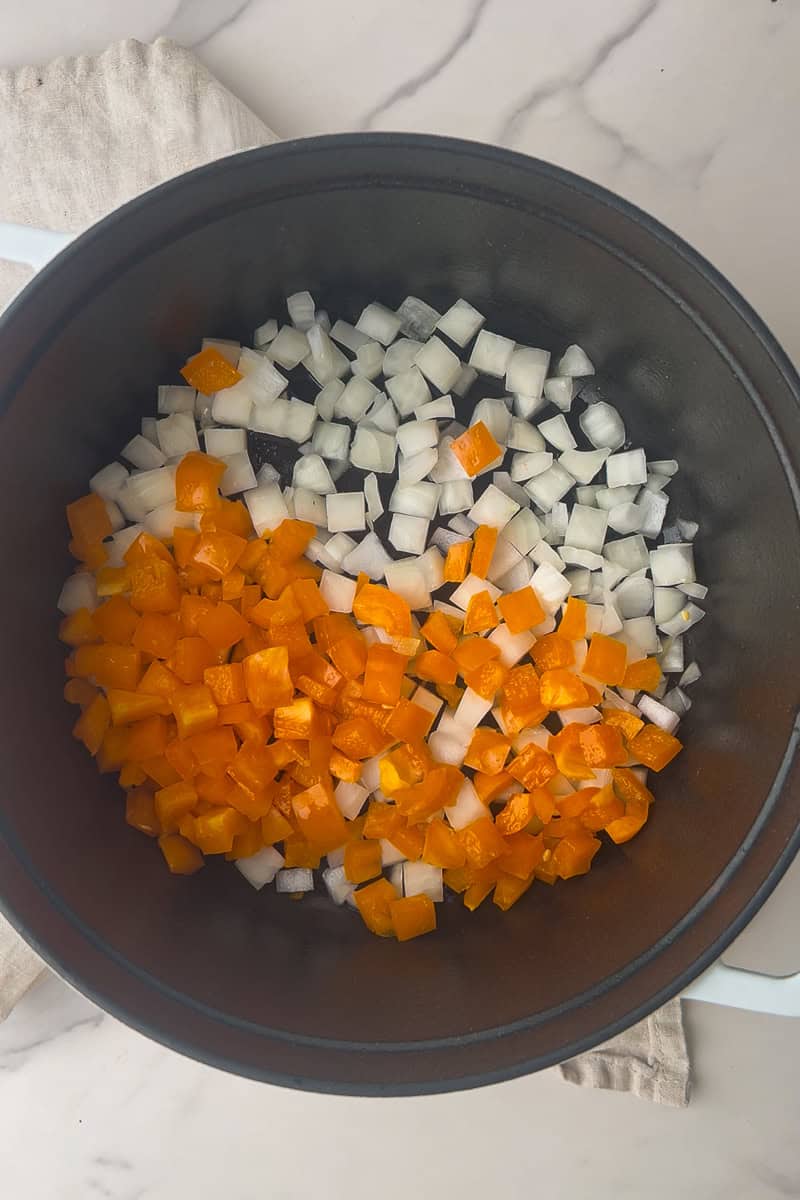 Diced orange bell pepper and white onion sit in a Dutch oven before sautéing.