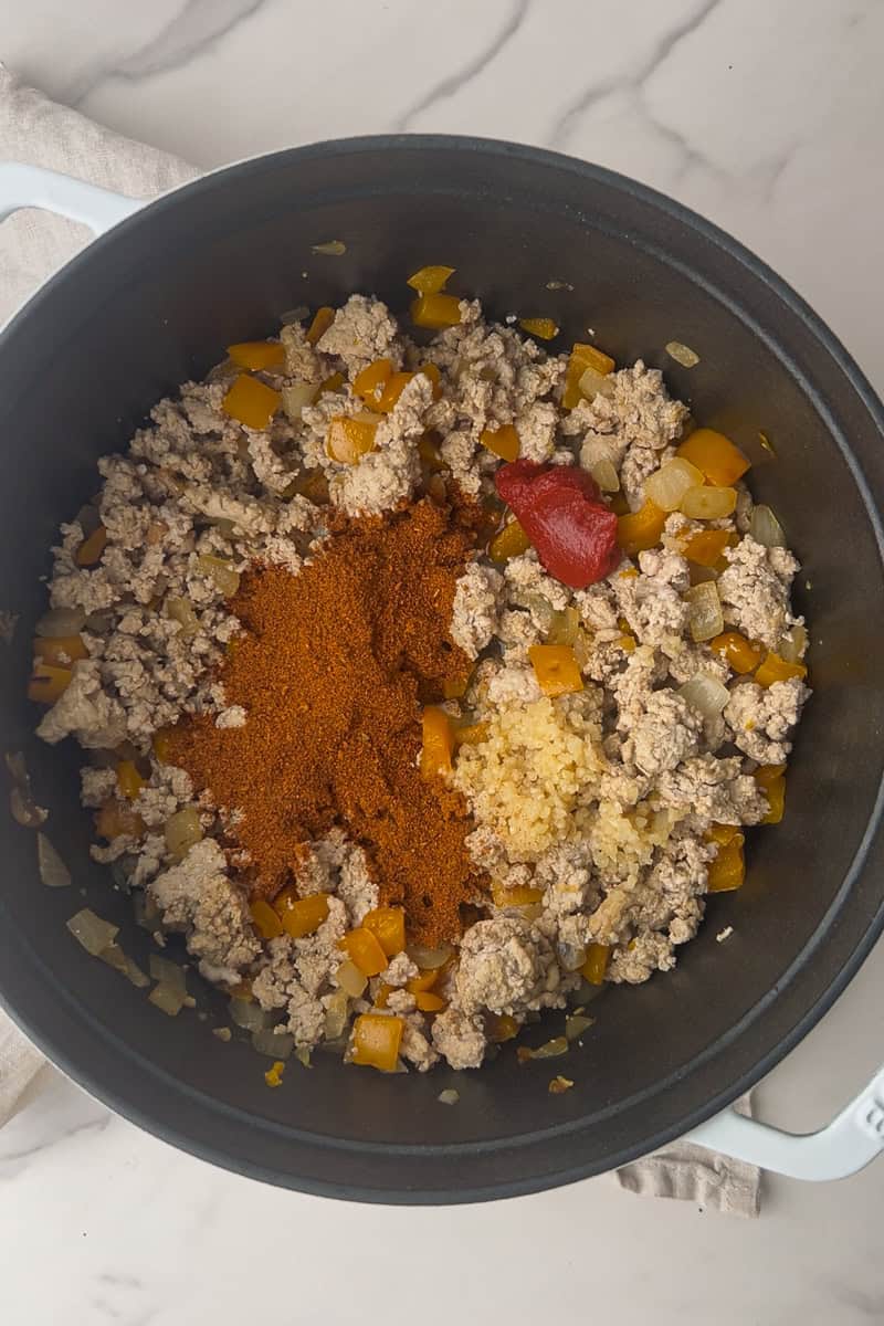Tomato paste, chili seasoning, and minced garlic are added on top of the cooked meat and veggies.