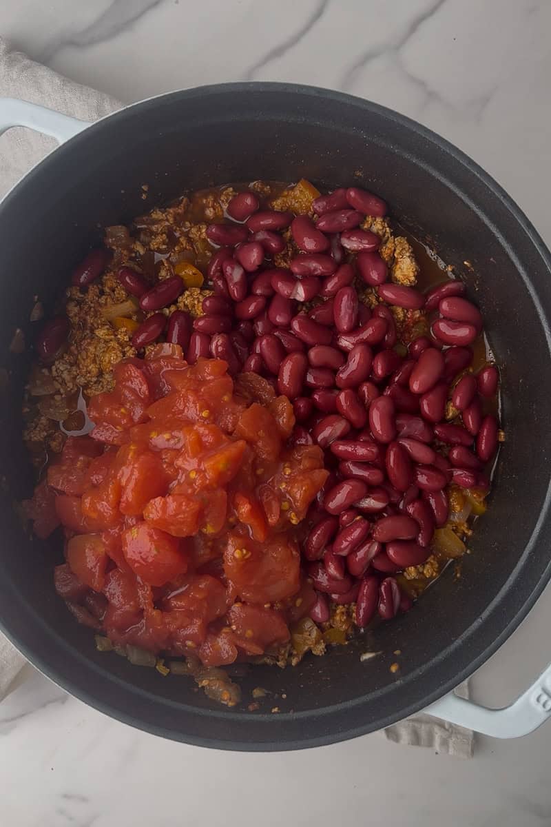 Kidney beans and diced tomatoes are poured into the Dutch oven with the seasoned meat mixture.