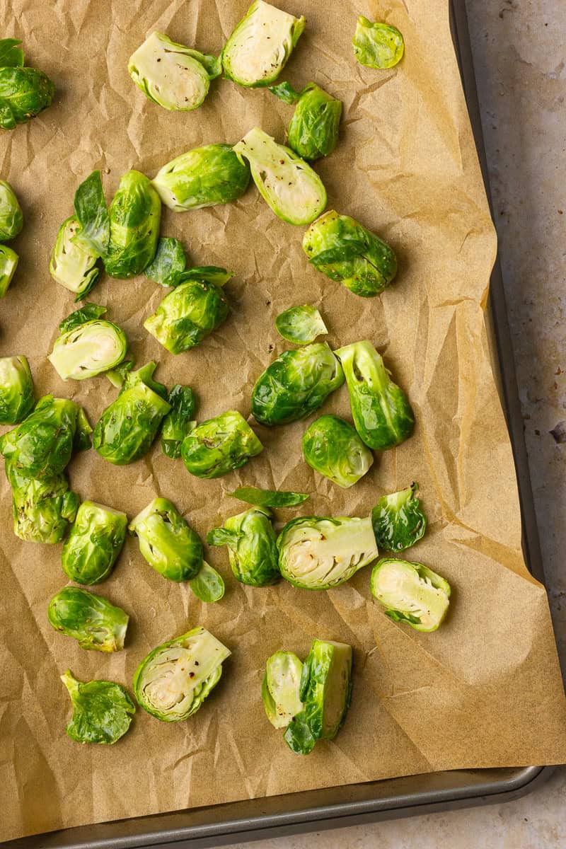 Seasoned Brussels sprouts are arranged on a parchment lined sheet pan ready to roast.
