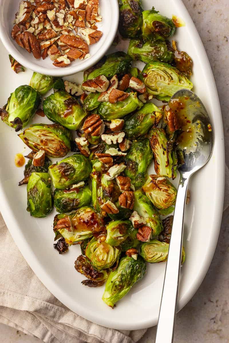 Roasted hot honey Brussels sprouts are plated with chopped pecans and a serving spoon.