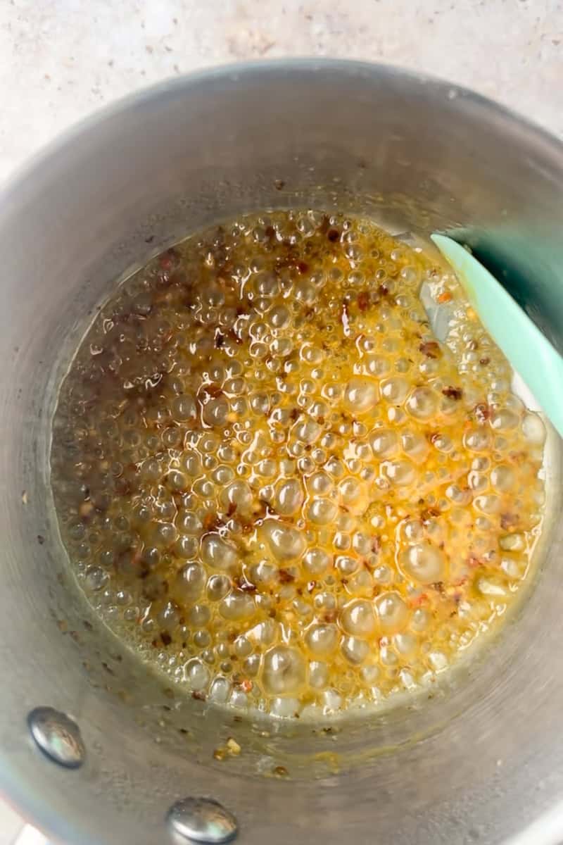 Bubbling hot honey Dijon butter with red pepper flakes simmers in a small saucepan.