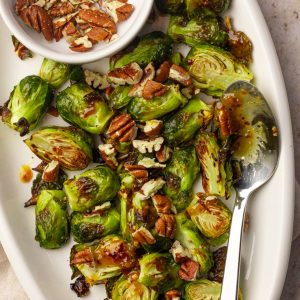 Platter of hot honey Brussels sprouts with chopped pecans and a spoon styled for serving.