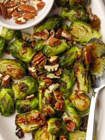 Platter of hot honey Brussels sprouts with chopped pecans and a spoon styled for serving.