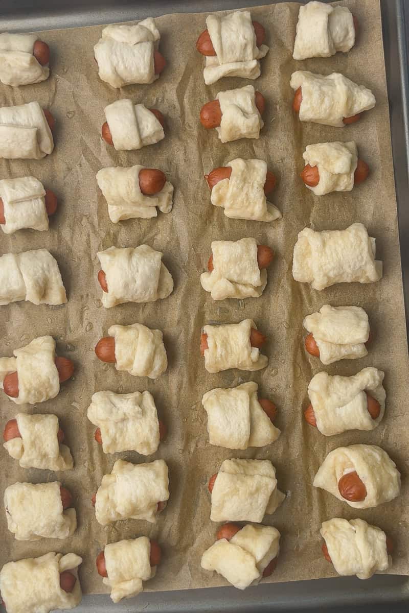 Tray lined with parchment showing wrapped mini pretzel dogs arranged before baking.