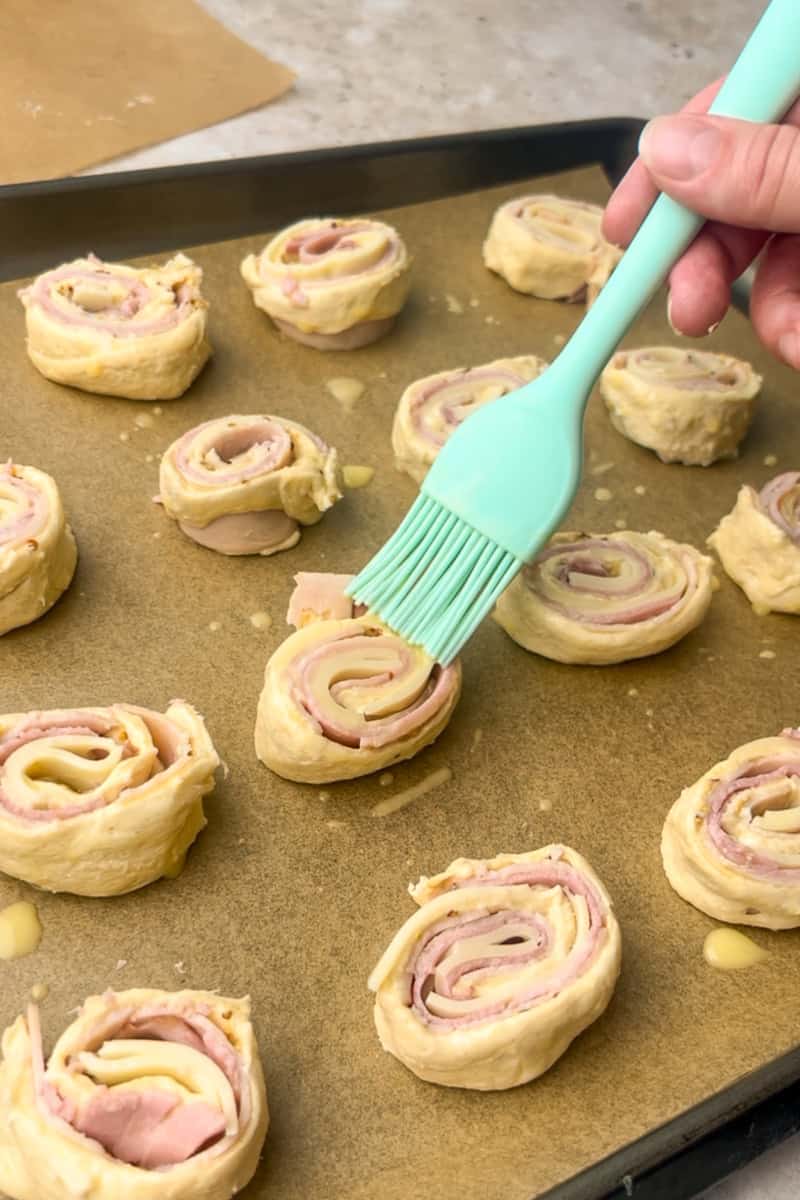 Pinwheel slices on a parchment-lined sheet pan are brushed with egg wash before baking.