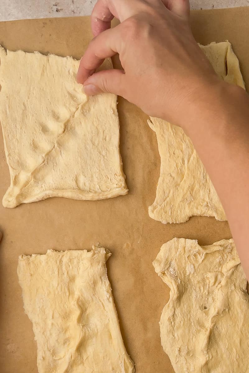 Crescent dough pieces are laid out on parchment while seams are pressed together to form rectangles.