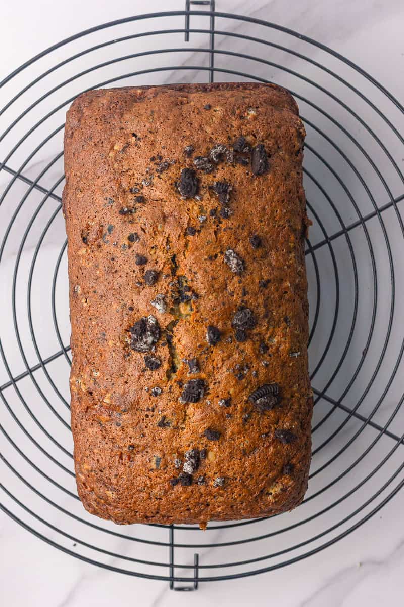 Overhead shot of the unglazed Oreo banana bread cooling on a wire rack with cookie bits on top.