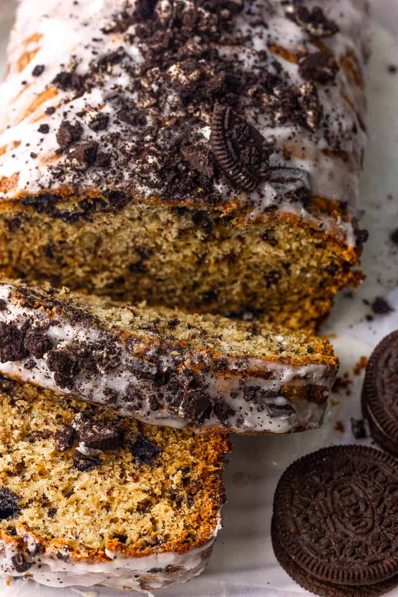 Sliced Oreo banana bread shows a tender crumb under a glaze and cookie crumble.