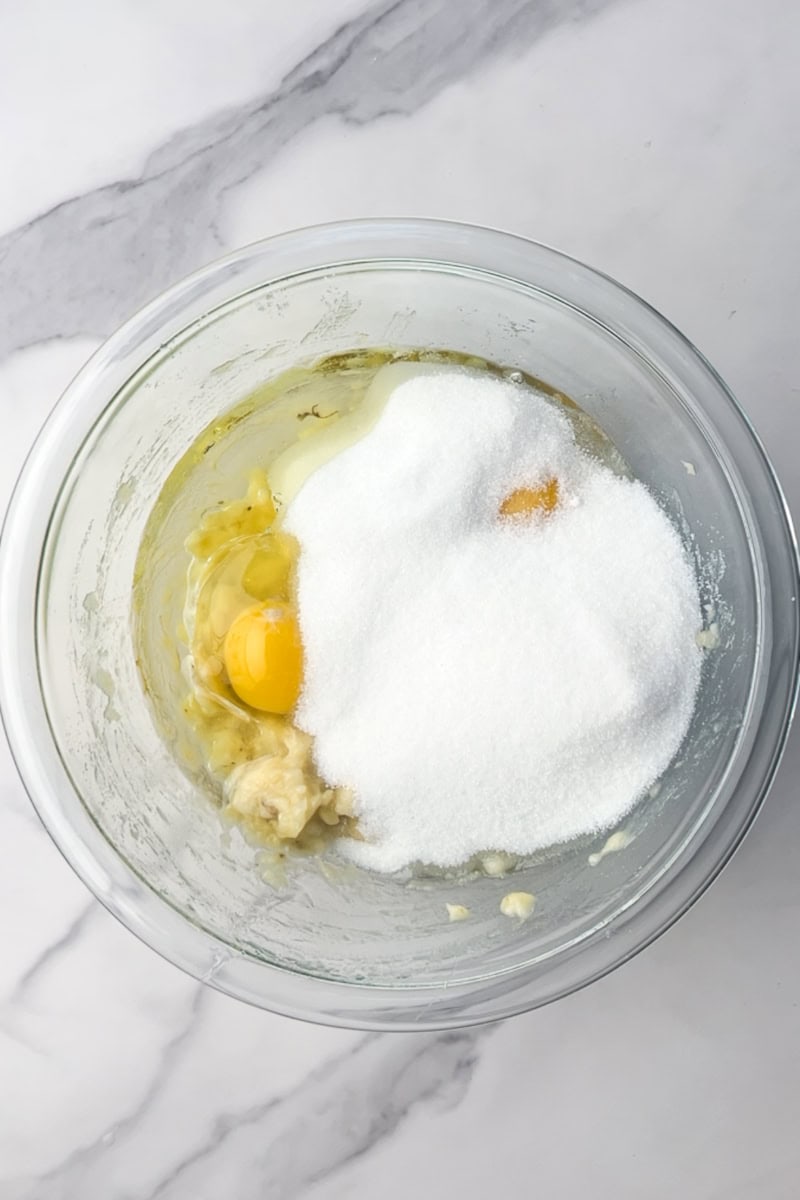 Mixing bowl holds mashed bananas, eggs, oil, and sugar before whisking.