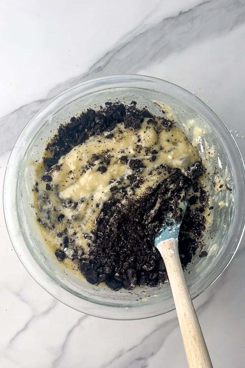 Crushed Oreos are being folded into the banana bread batter with a spatula.
