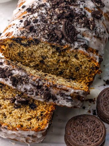 Glazed Oreo banana bread topped with crushed cookies, sliced to show the cookie-studded crumb.
