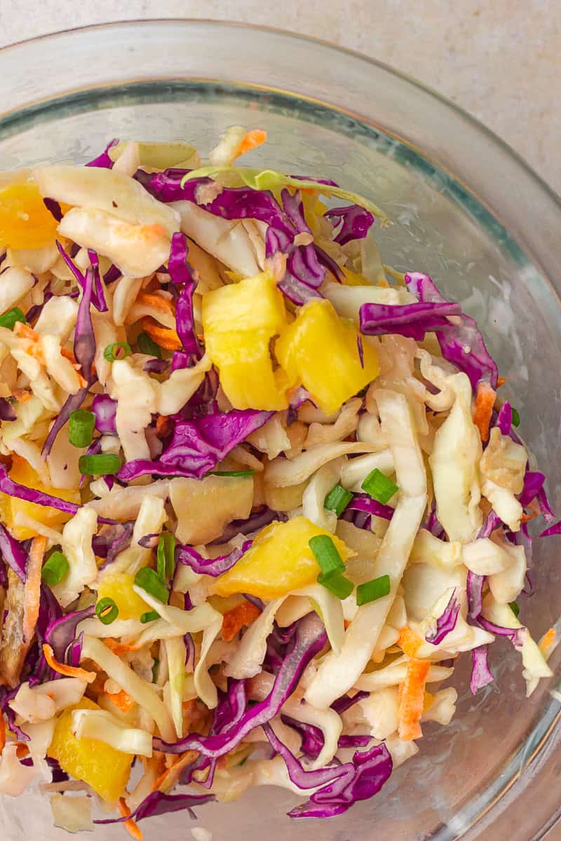The tossed pineapple slaw shows cabbage, pineapple, and green onions in a clear bowl.