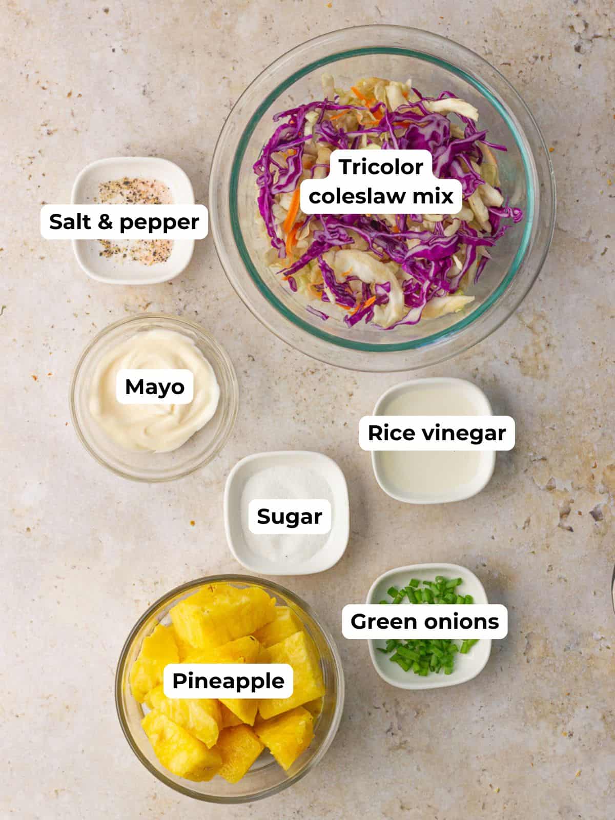 A flat lay displays coleslaw mix, pineapple, mayo, sugar, rice vinegar, and green onions.