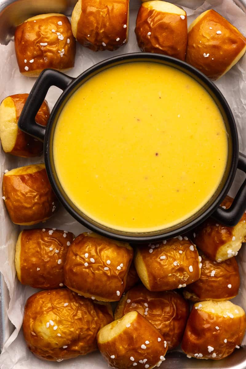 A black bowl of golden pretzel cheese dip surrounded by soft pretzel bites topped with salt.
