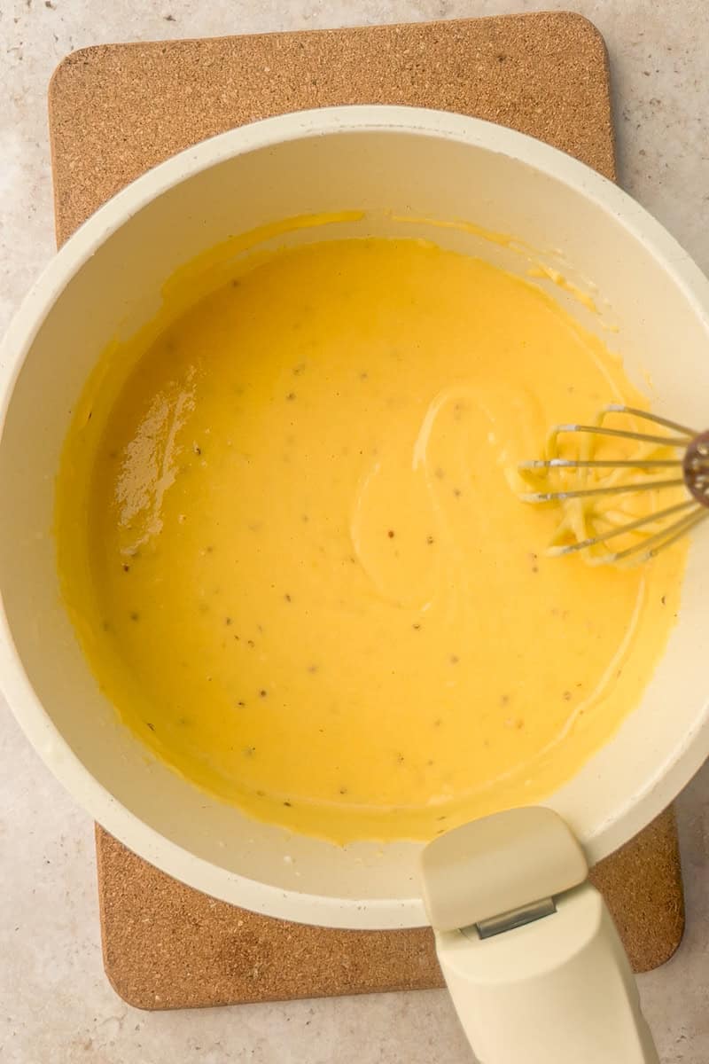 Cheese, mustard, and hot sauce added to the milk mixture in a saucepan before whisking.