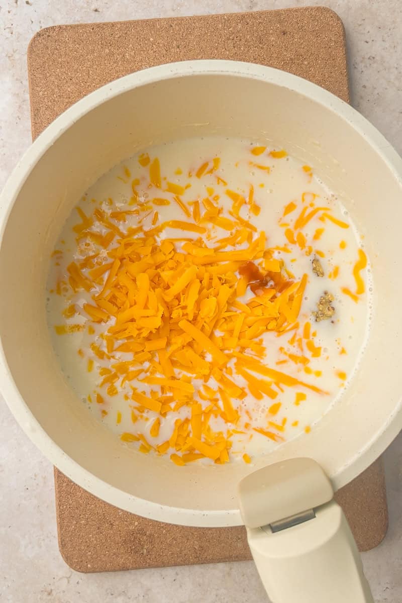 Saucepan with melted cheddar cheese and seasonings being whisked into a creamy sauce.