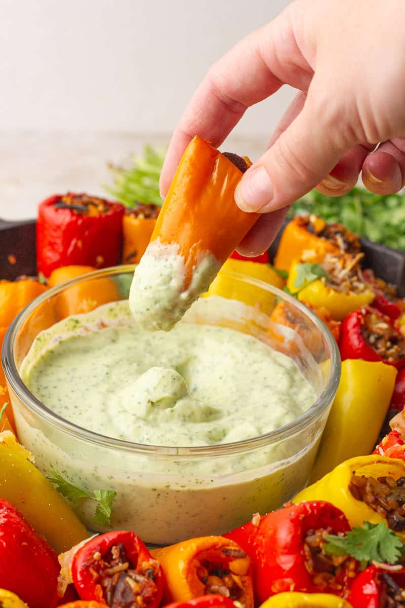 A hand dips a stuffed mini pepper into a bowl of creamy green sauce.