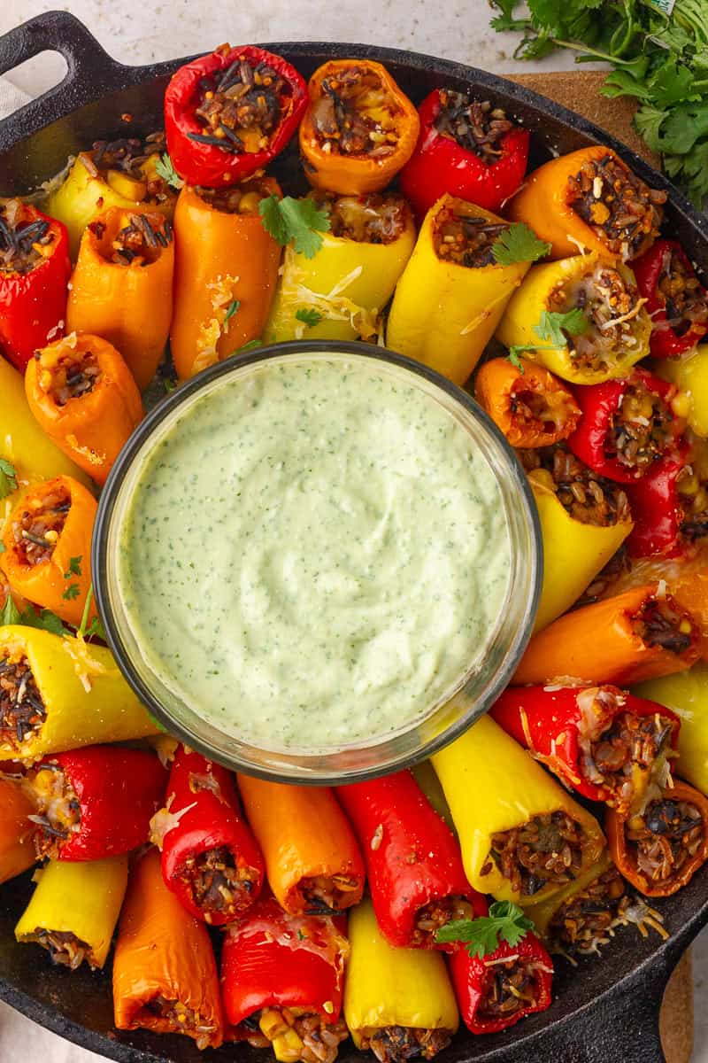 Rice-stuffed mini peppers circle a bowl of green dip in a tight top-down view of the skillet.