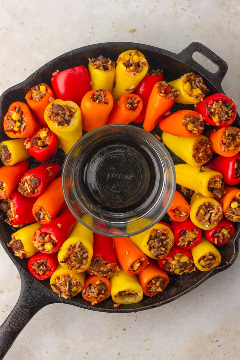 Stuffed mini peppers are arranged in a ring around an empty clear bowl to reserve space for dip in the skillet.