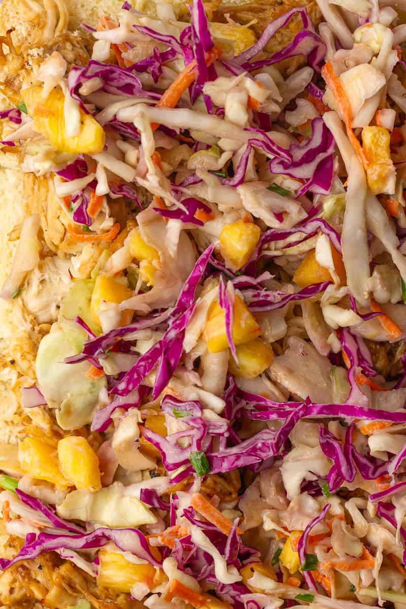 A close-up shows pineapple slaw piled on teriyaki chicken slider filling with purple cabbage and pineapple pieces.
