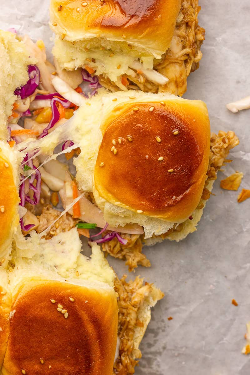 Pull-apart Hawaiian roll sliders reveal melty cheese stretch with slaw and sesame seeds.