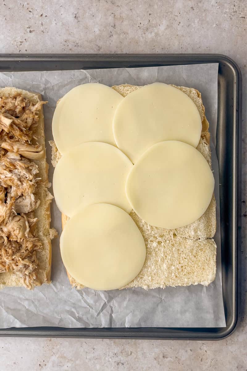 The bottom slab of rolls is topped with sauced shredded chicken while the top slab shows cheese slices.