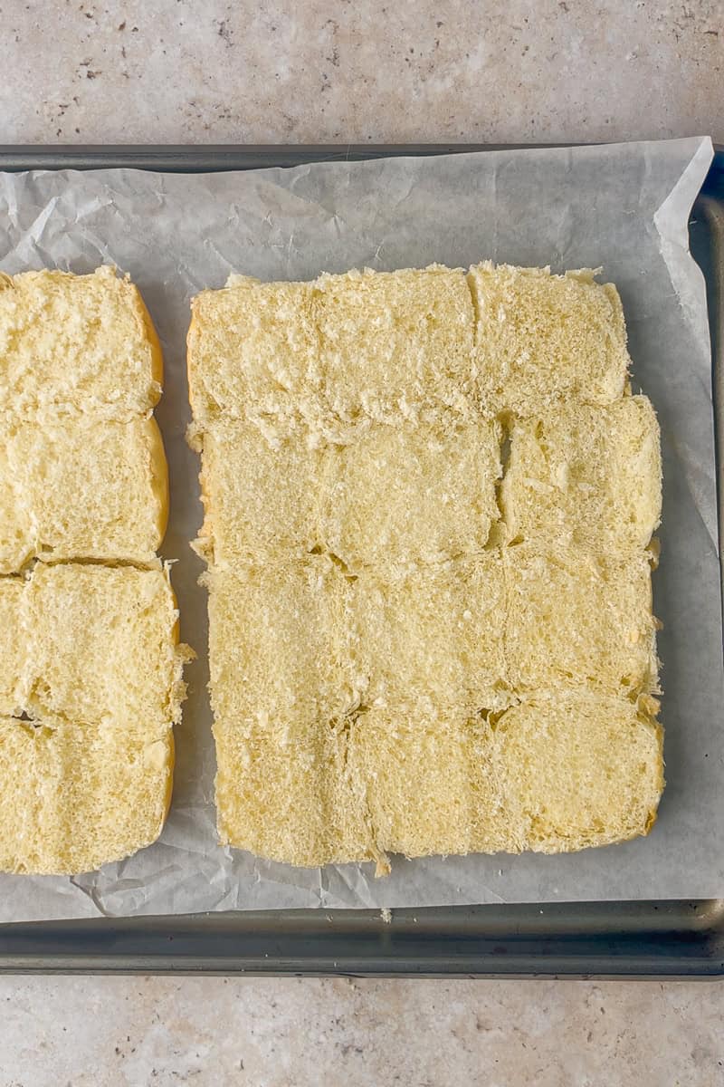 The sliced bottom slab of 12 Hawaiian rolls sits on a parchment-lined baking sheet.