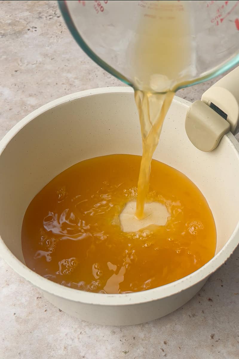 Apple cider is poured from a measuring cup into a saucepan to start the caramel.