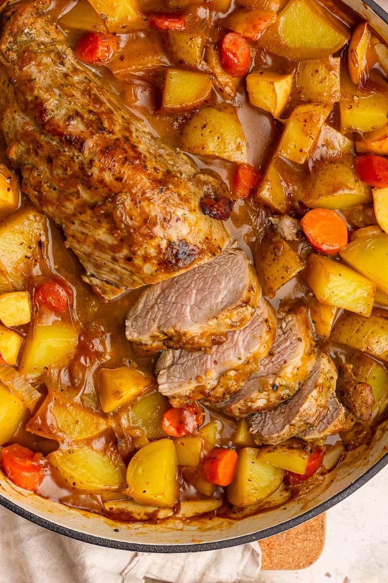 Sliced apple cider pork tenderloin in a braiser with carrots, potatoes, and rich cider sauce.
