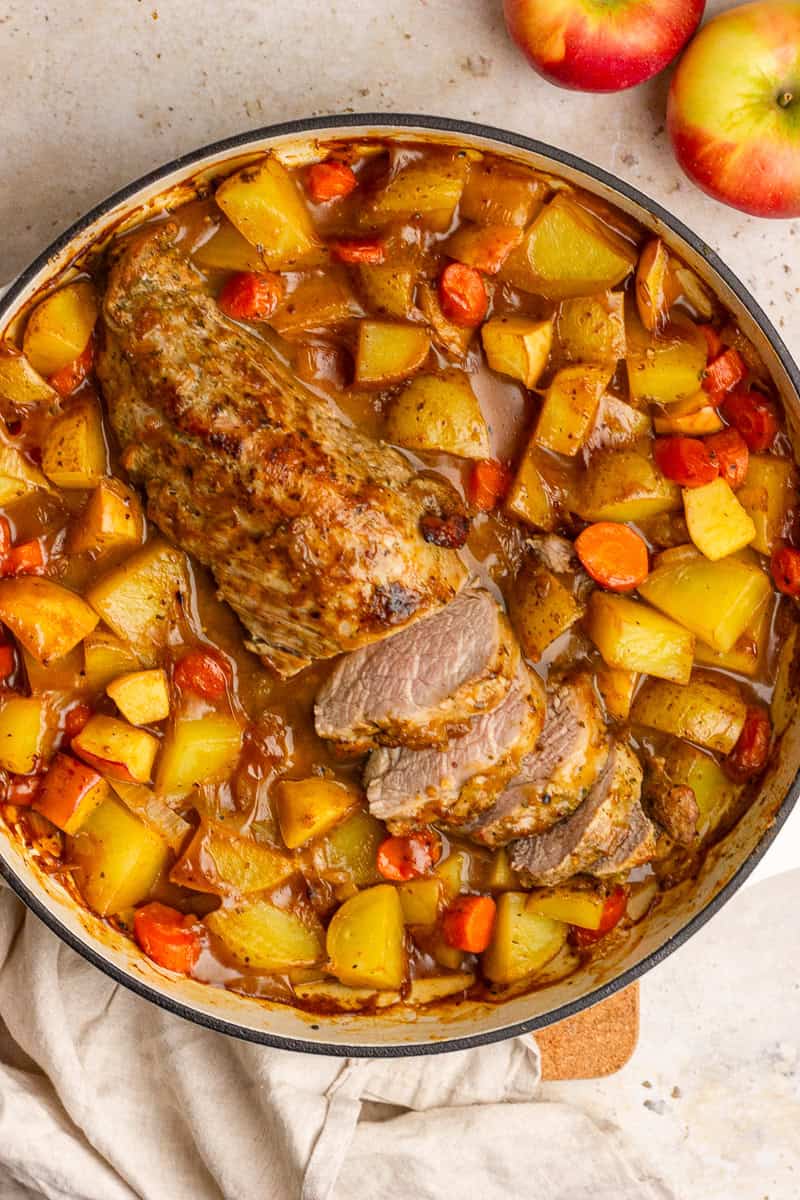 Sliced apple cider pork tenderloin in a braiser pan with carrots and potatoes in rich sauce.