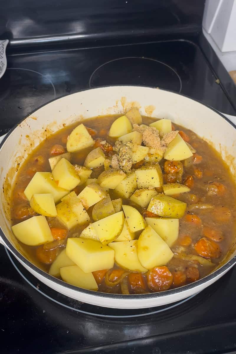 Potatoes and carrots simmering in apple cider sauce inside a white braiser pan.