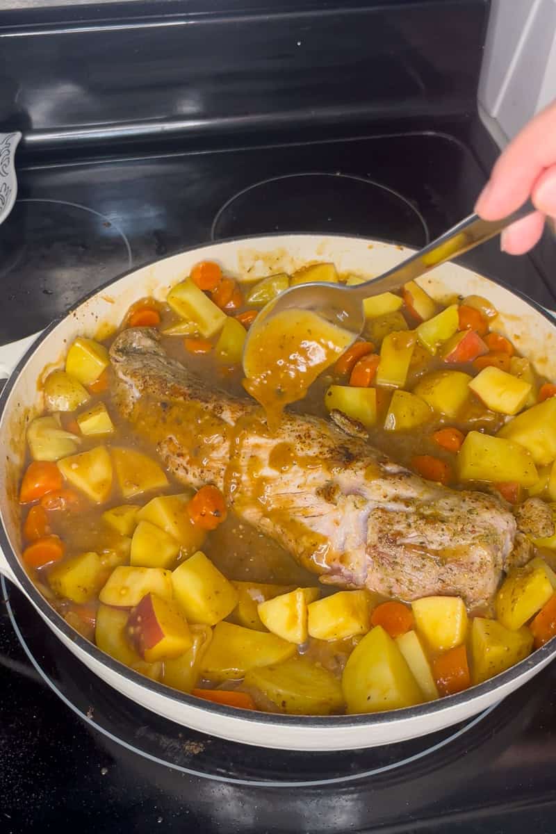 Pork tenderloin with vegetables simmering in apple cider sauce before baking.