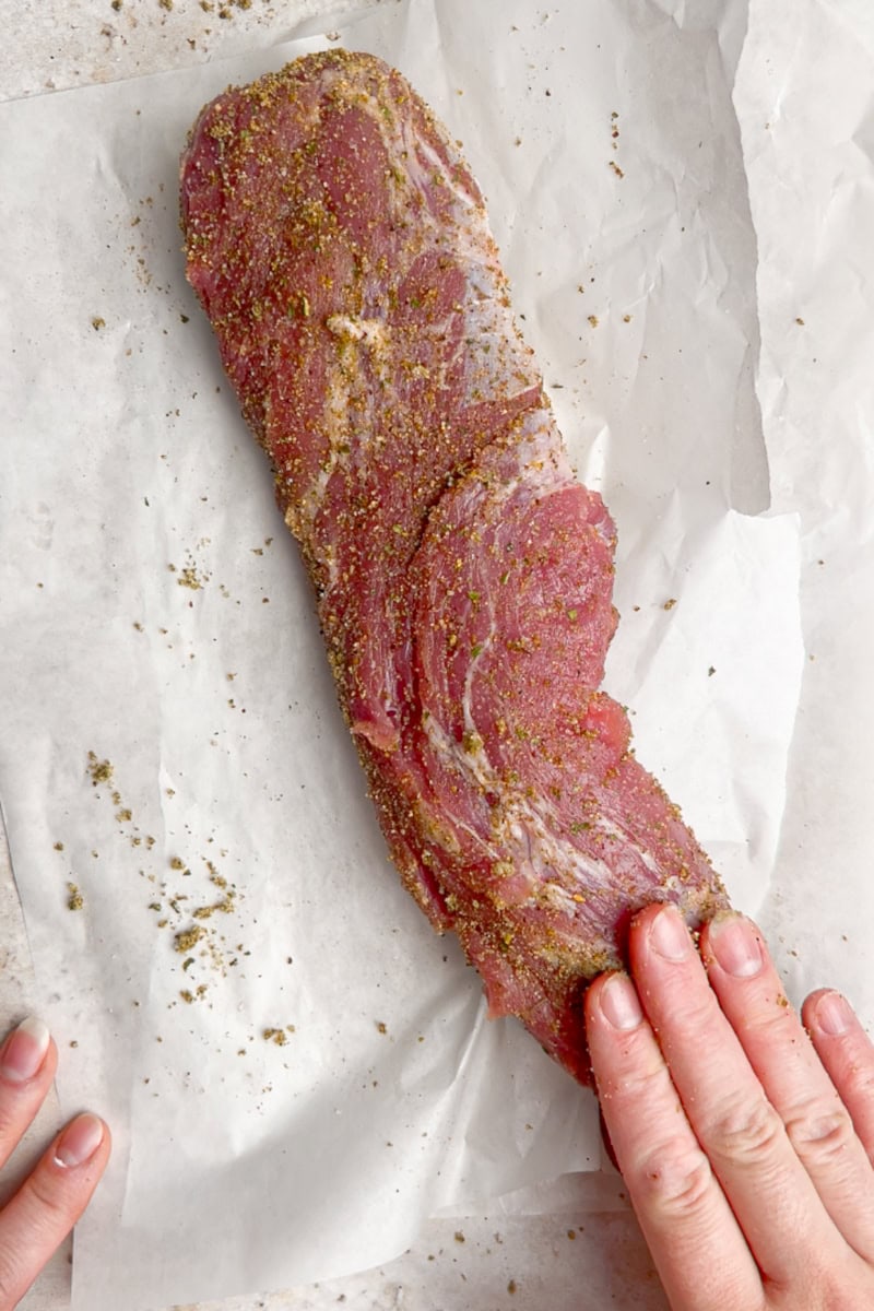 Pork tenderloin being coated with herb seasoning mixture before cooking.