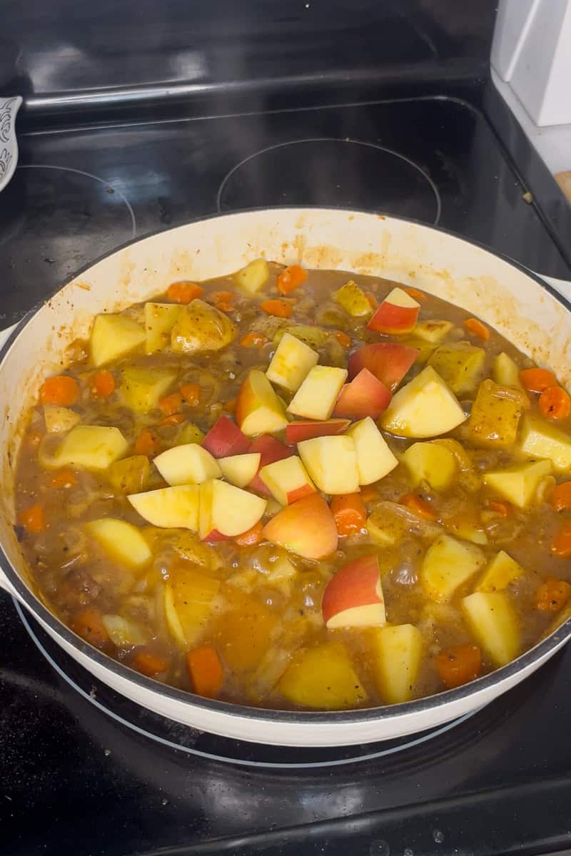 Diced apples added to simmering potatoes and carrots in apple cider sauce.
