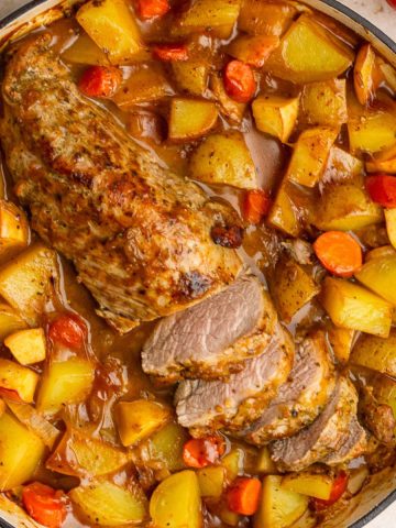 Overhead view of apple cider pork tenderloin surrounded by roasted potatoes and carrots.